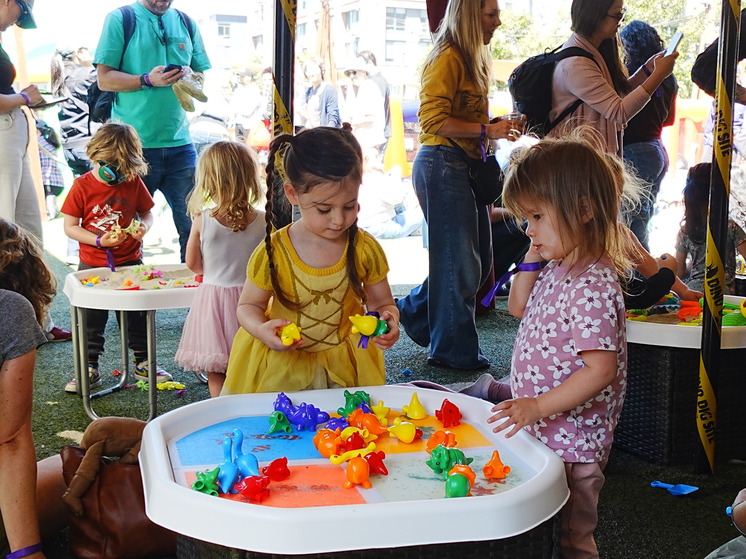 Children playing with colorful toys at a table in a crowded outdoor event.