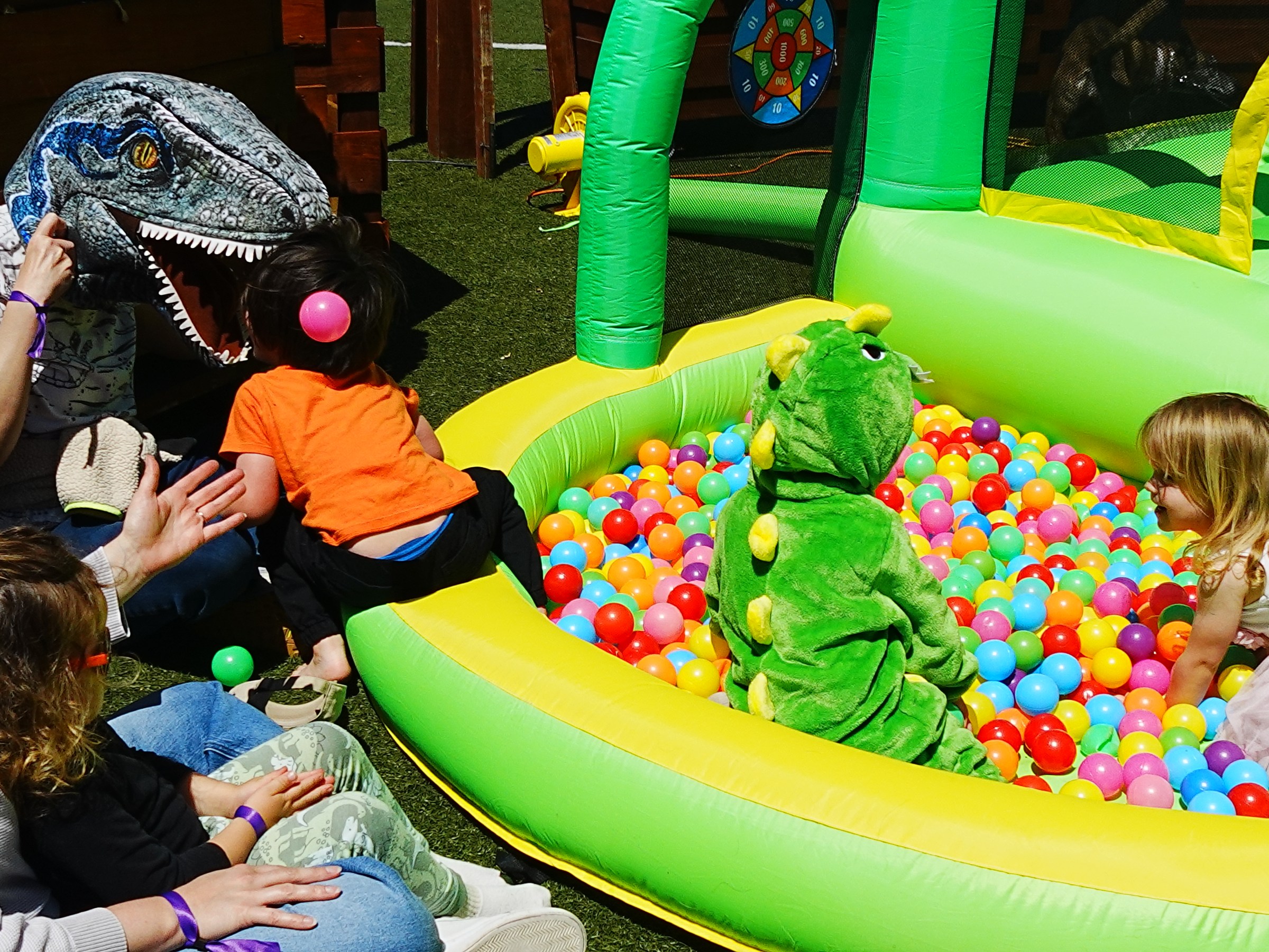 Kids playing in ball pit, inflatable dinosaur costume nearby.