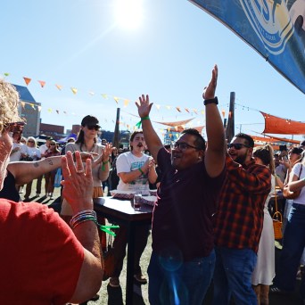 People celebrate outdoors under colorful banners and sunlight.