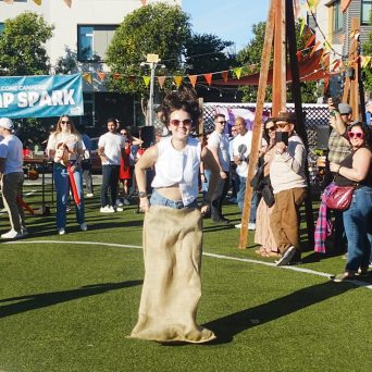 Person in a sack race at an outdoor festival with audience watching.
